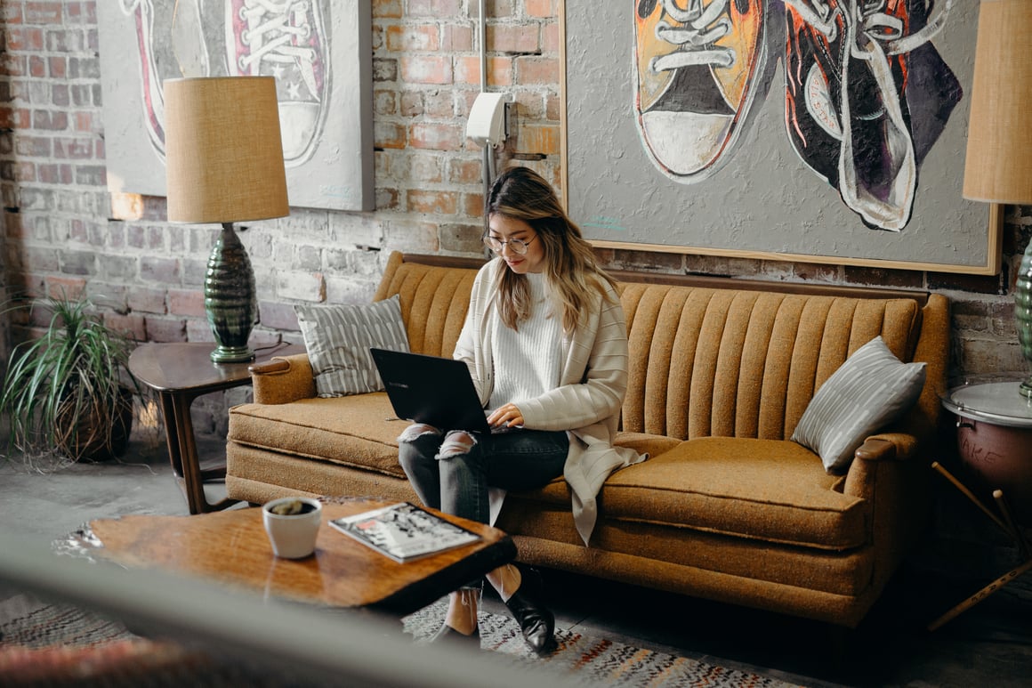 Woman sitting on couch typing on laptop.