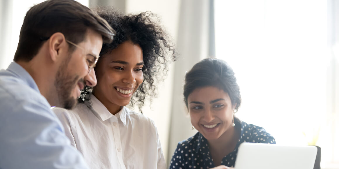 A man and two women looking over a sales deal on a computer smiling. 