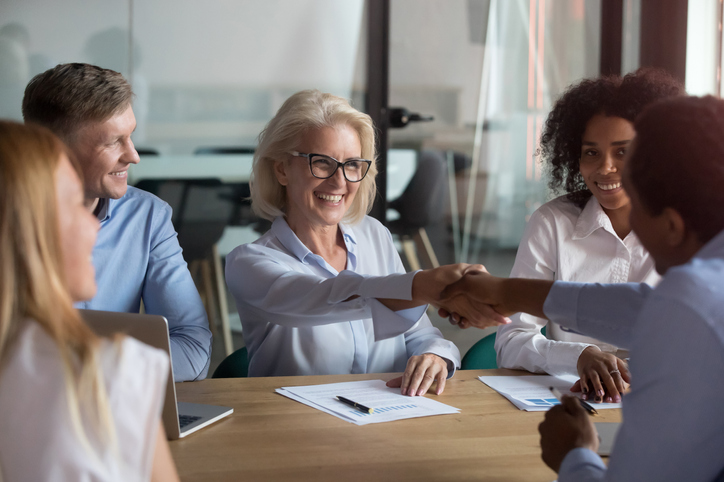 Customer success team in action at table with clients shaking hands.